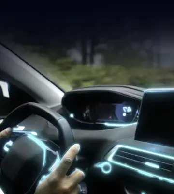 Hands on steering wheel with a front-view of the dashboard illuminated in neon blue accents.