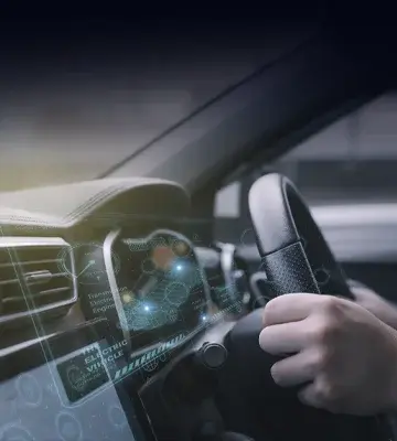 Hands on steering wheel with an electronic overlay on the dashboard.