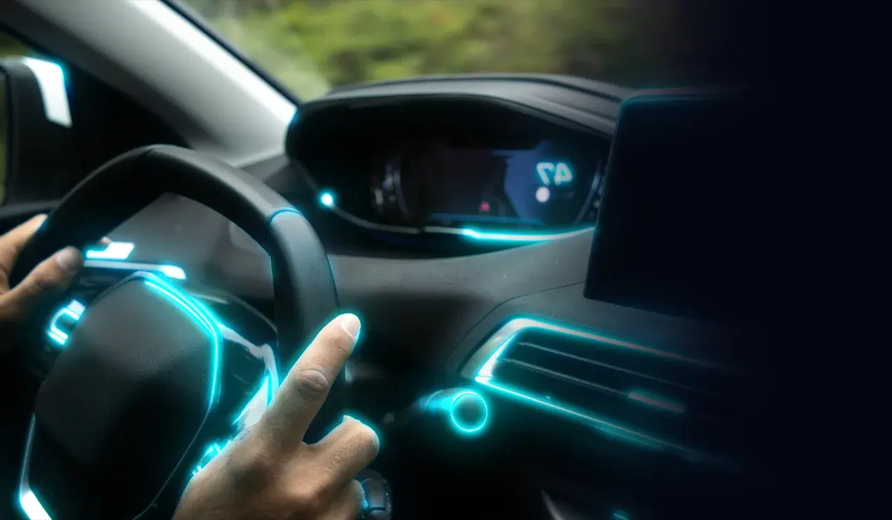 Hands on steering wheel with a front-view of the dashboard illuminated in neon blue accents.